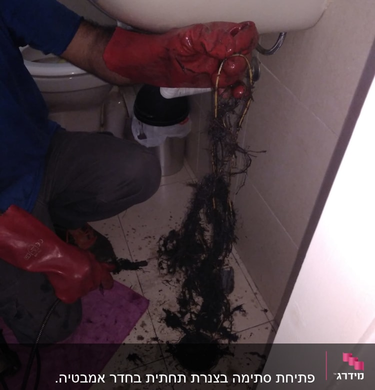 אינסטלטור עם כפפות אדומות מנקה סתימה בכיור